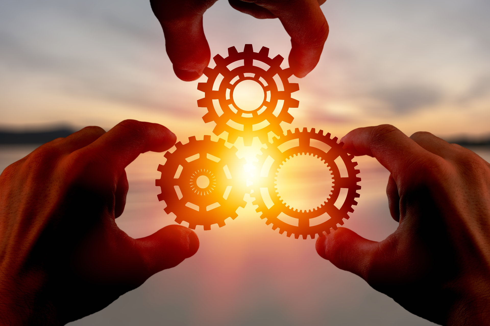 Four hands joining interlocking gears against a bright sky